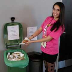 Young woman smiling at camera and placing paper item into open compost collection bin.