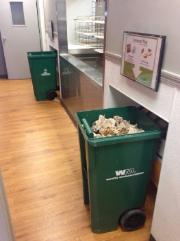Waste Management bins in a hallway with signage on the wall above them.